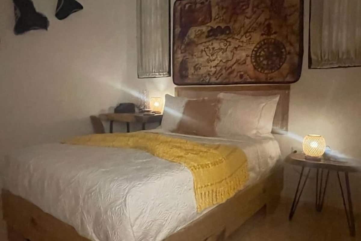 A bedroom with a wooden bed, a large wall map, and a small bedside table with a lamp.