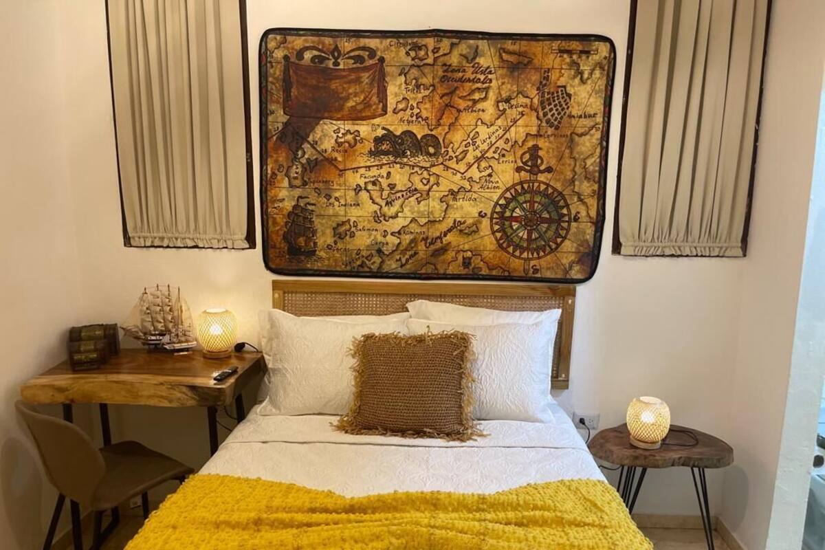 A bedroom with a large bed, a wooden nightstand, a desk, and a map artwork on the wall.