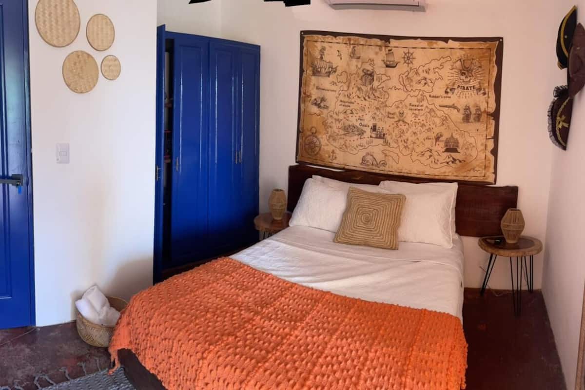 A bedroom with a bed, a blue door, a map on the wall, and a small round table.