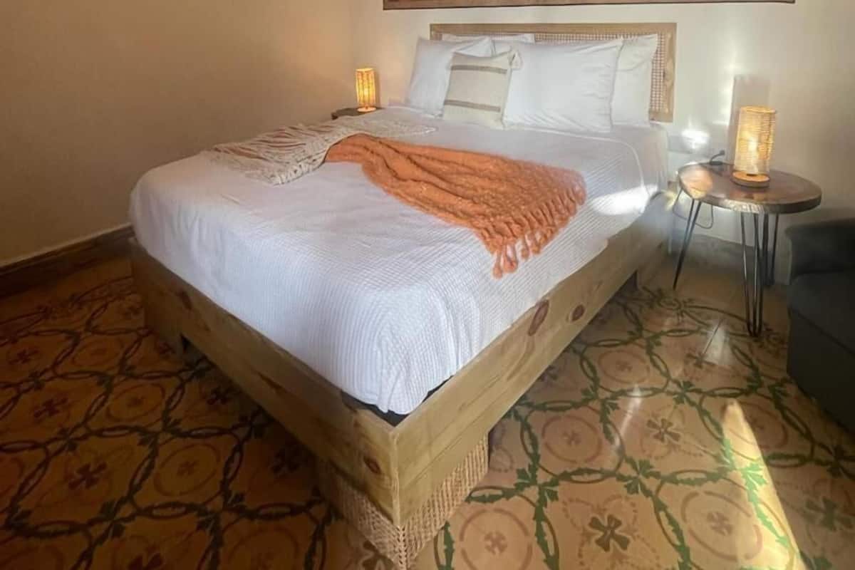 A hotel room with a large bed, a small side table, a decorative wall hanging, and patterned flooring.