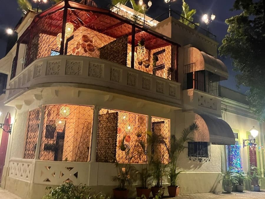 Un edificio de dos pisos con un balcón, plantas en macetas e iluminación decorativa.