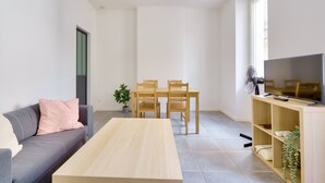 A modern living room with a sofa, coffee table, dining table, chairs, a TV, and a fan. - Charming apartment located 10 min from the seaside (Marseille)