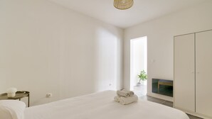 A minimalist bedroom with a large bed, a bedside table, a wardrobe, and a view of a balcony with a plant. - Charming apartment located 10 min from the seaside (Marseille)