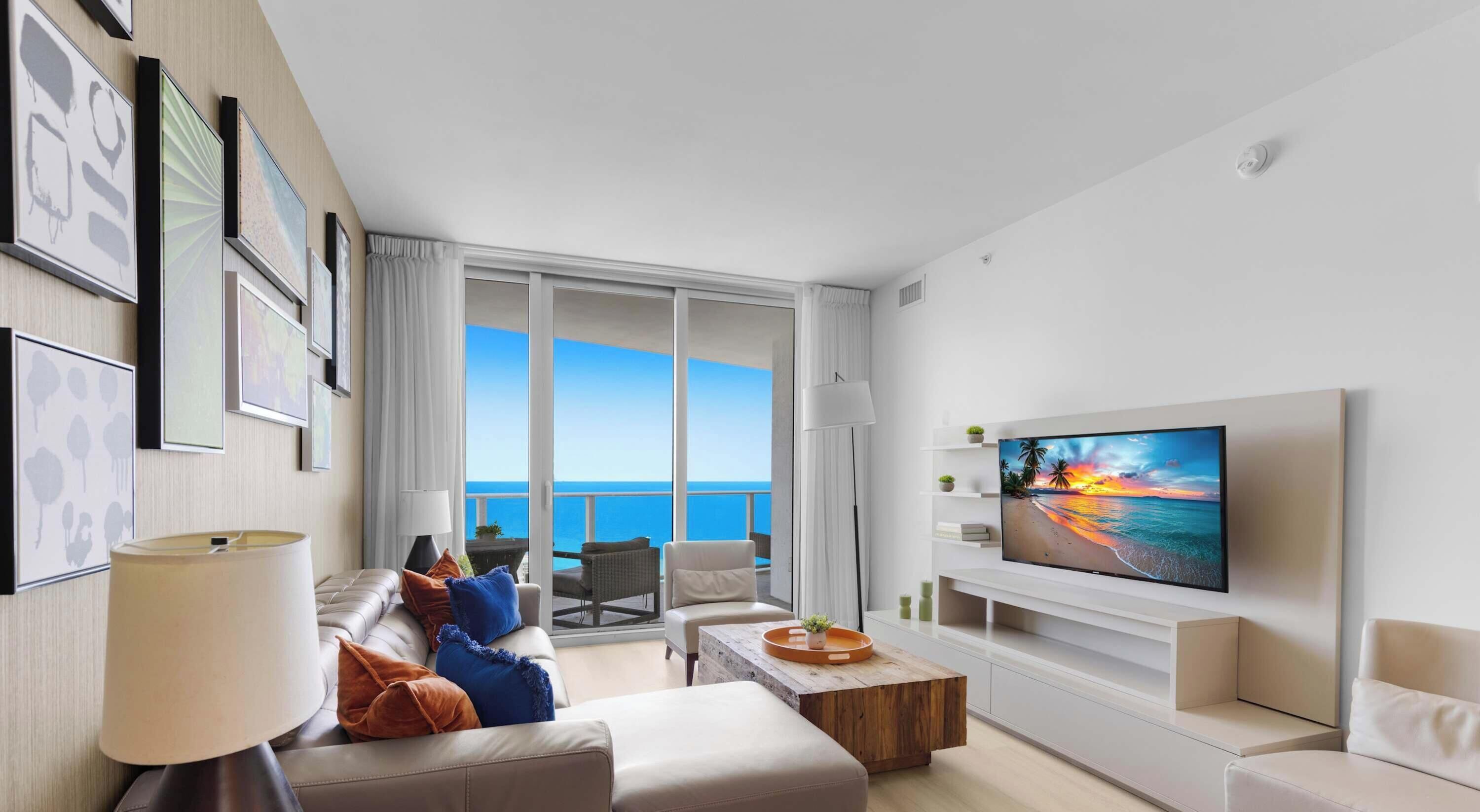 Un salon moderne doté d’un grand téléviseur, de sièges confortables et d’un balcon offrant une vue sur la mer.