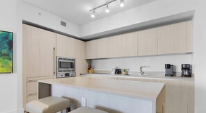 Uma cozinha moderna com armários de madeira clara, micro-ondas embutido, máquina de café e pia.