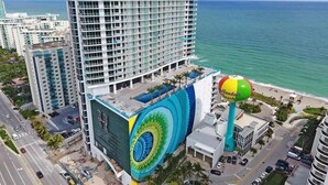 Un hotel de gran altura con un mural grande en la fachada, una pelota de playa y vista al océano.