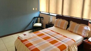 A hotel room with a bed, a chair, a nightstand, and a window with curtains. - Villa Garza Inn (Guayaquil)