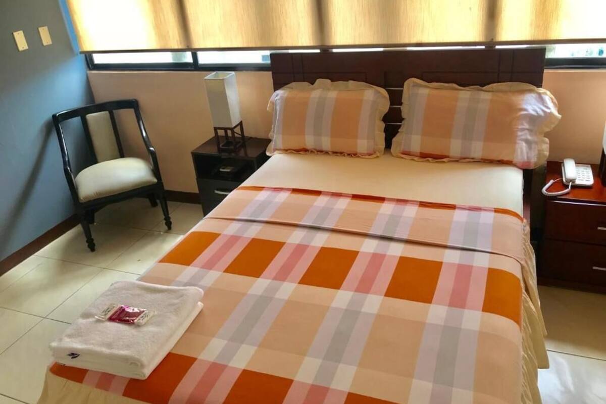 Une chambre d’hôtel avec un lit, une chaise, une table de chevet et une fenêtre avec des rideaux.