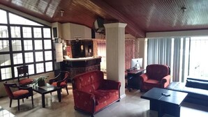 A spacious lobby with a red sofa, a coffee table, and a seating area with chairs. There is a reception desk with a computer and a clock. The room has large windows and a high ceiling with wooden beams. - Villa Garza Inn (Guayaquil)