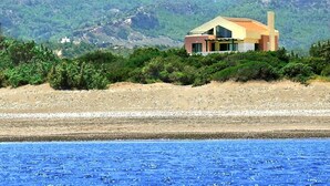 Ett hus vid kusten med modern design, beläget på en sluttning med utsikt över havet och berg i bakgrunden.