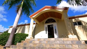 A building with a stone staircase leading to a door with glass panels, surrounded by palm trees.