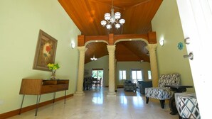 A spacious living area with high ceilings, a chandelier, and a dining area in the background.