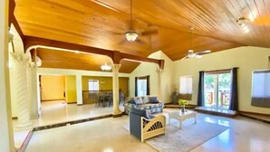 A spacious living area with a high ceiling and wooden beams, a sofa, a coffee table, and a view of the outdoors.