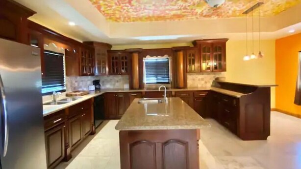 A modern kitchen with wooden cabinets, a central island, and a ceiling with a floral pattern.