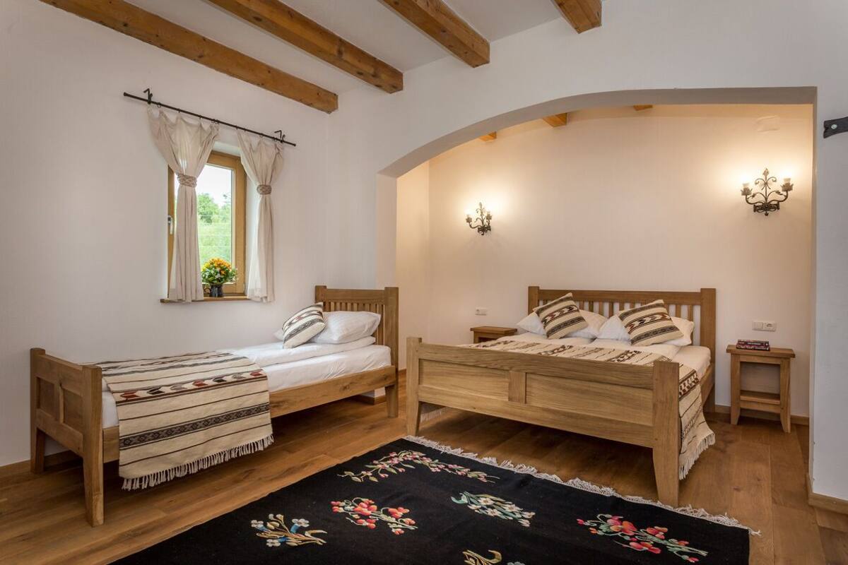 A bedroom with two wooden beds, a window with curtains, a floral rug, and wall-mounted lights.