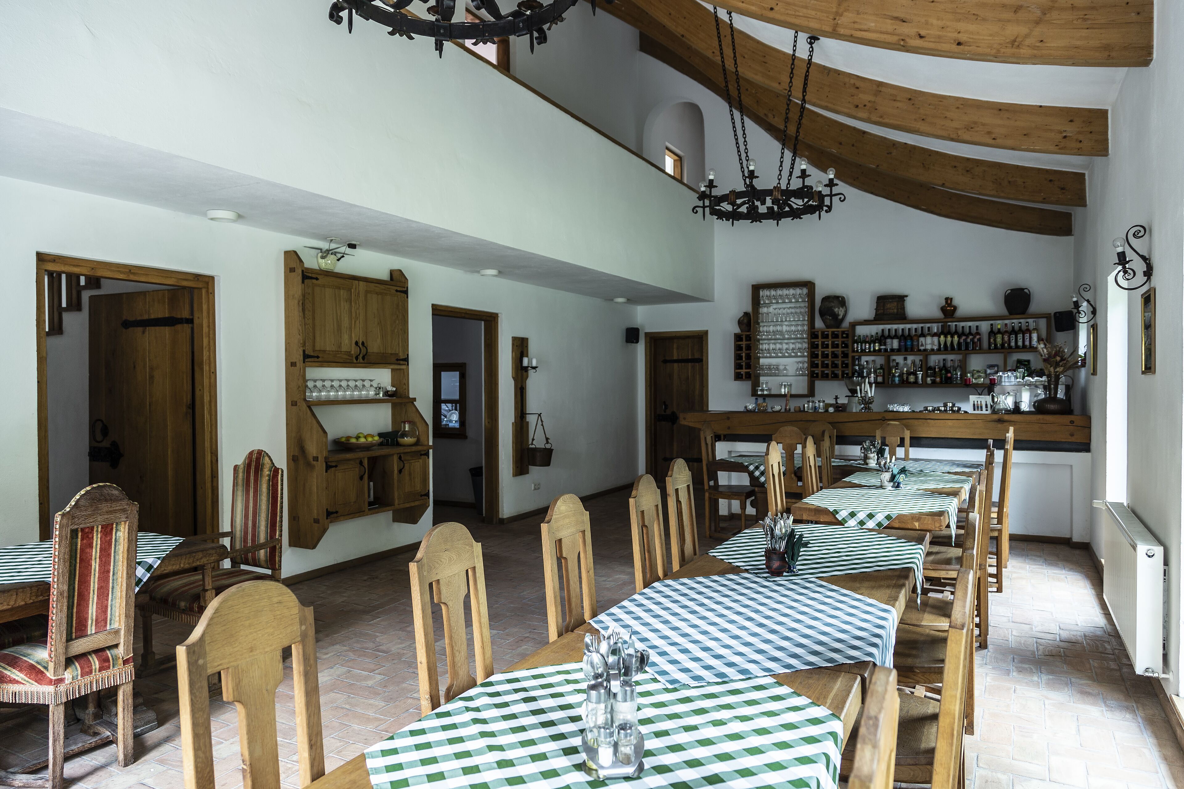 Uma sala de jantar com mesas e cadeiras de madeira, um candelabro e um espaço de bar com prateleiras cheias de garrafas.