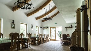 A dining hall with wooden tables and chairs, a chandelier, and a hanging pot. - Hanul Vatra (Costesti)