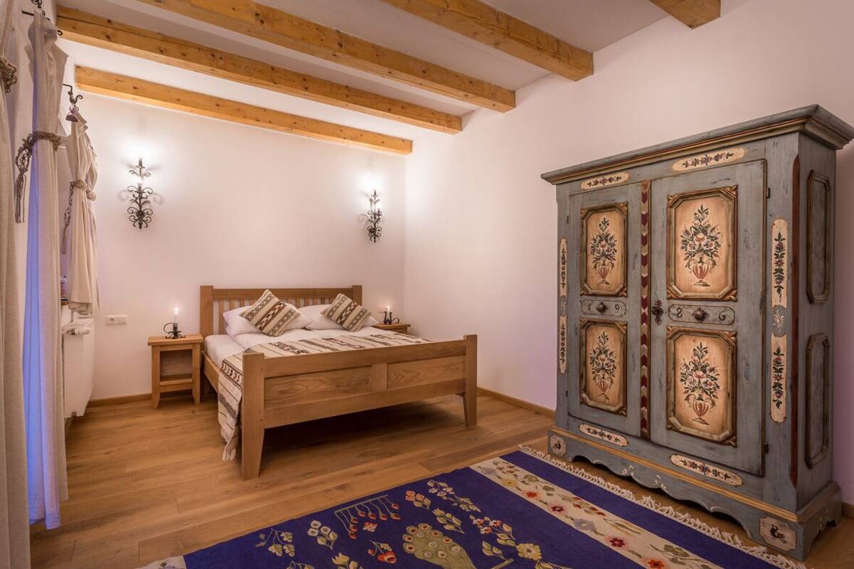 A bedroom with a wooden bed, a nightstand, a blue cabinet with floral designs, and a patterned rug.