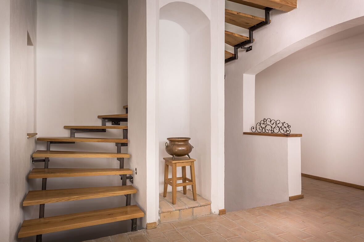 Una escalera con escalones de madera y soportes metálicos, que lleva a una plataforma con una maceta sobre un taburete y un estante metálico decorativo.