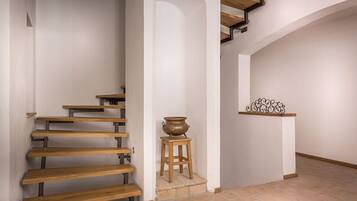 Una escalera con escalones de madera y soportes metálicos, que lleva a una plataforma con una maceta sobre un taburete y un estante metálico decorativo.