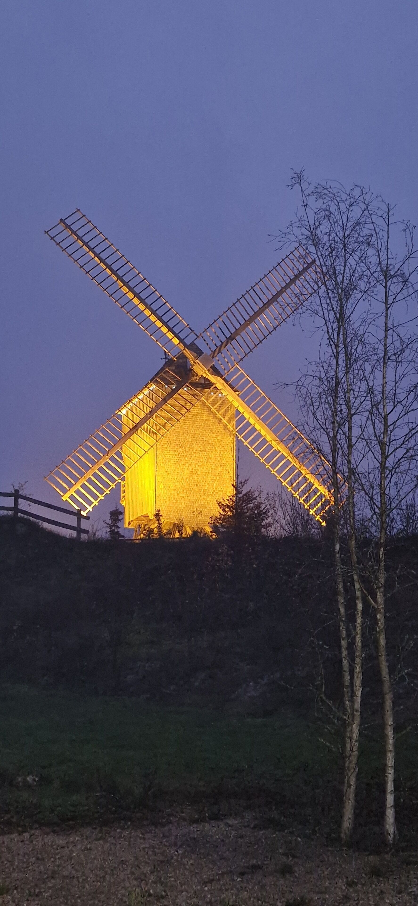 Eine Windmühle mit einer großen, beleuchteten Struktur, umgeben von Bäumen und einer grünen Wiese.