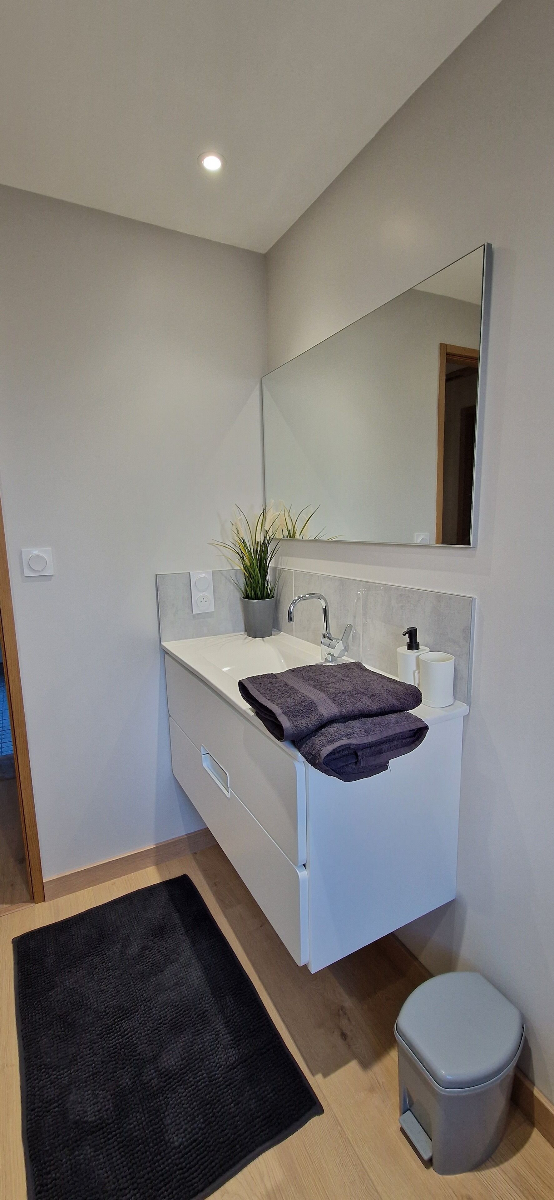 Un bagno moderno con un mobile lavabo bianco, uno specchio grande, un lavandino, un water e un tappeto nero.