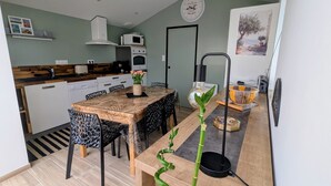 Une cuisine compacte avec des meubles blancs, un four à micro-ondes et une cuisinière. On y trouve une table à manger avec des chaises et un vase rempli de fleurs.