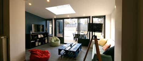A modern living room with a flat-screen TV, a bean bag, a wooden table, and a tripod.
