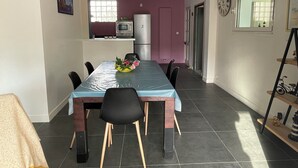 Un coin repas avec une table dressée pour six personnes, une cuisine en arrière-plan et une horloge au mur.