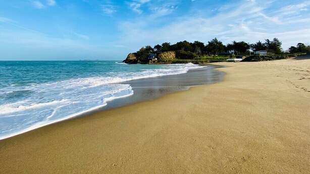 Une plage avec un ciel dégagé, une mer calme et une maison située sur une falaise.