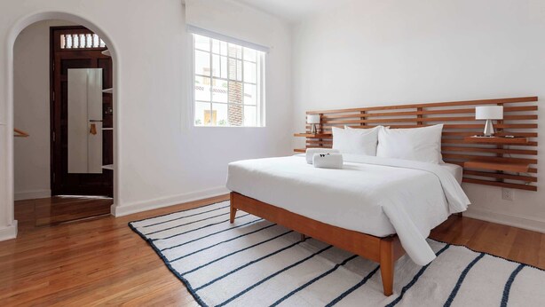 A bedroom with a wooden bed, white bedding, a striped rug, and a window with blinds. - w* | Elegant & Bright 2BR in Prime Polanco (Ciudad de México)