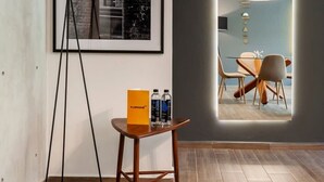 A modern hotel room with a large framed photograph on the wall, a small table with a tray of toiletries, and a view of a dining area through a semi-transparent archway. - w* | Refined 2BR w/ Balcony in Parque España (Ciudad de México)