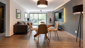 A modern living room with a dining area, large windows, and a flat-screen TV. - w* | Refined 2BR w/ Balcony in Parque España (Ciudad de México)
