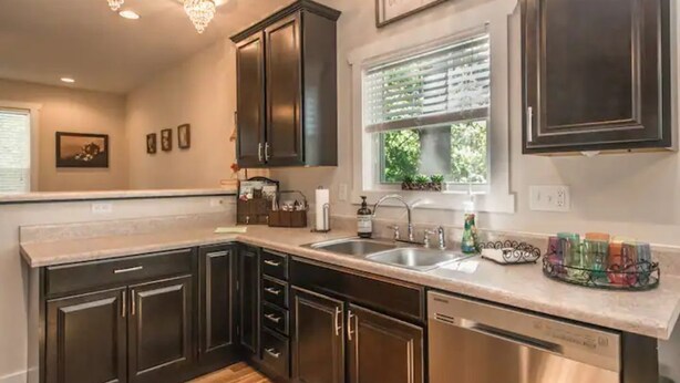 A modern kitchen with dark cabinetry, stainless steel appliances, and a large window with blinds. - Be our guest-3-bedroom house in a great location! (Fletcher)