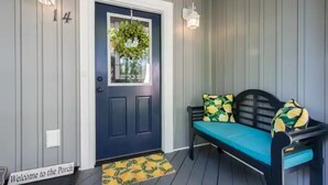 A porch with a dark blue door, a welcome sign, a bench with patterned cushions, and two wall-mounted lights. - Be our guest-3-bedroom house in a great location! (Fletcher)