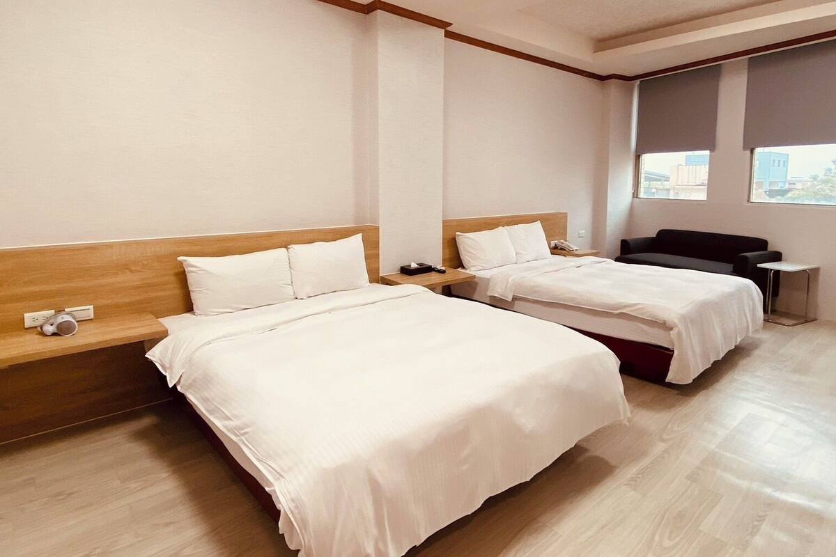 Ein Hotelzimmer mit zwei Betten, Holzkopfteilen, einem kleinen Nachttisch mit Telefon und einem Fenster mit Blick auf Gebäude.