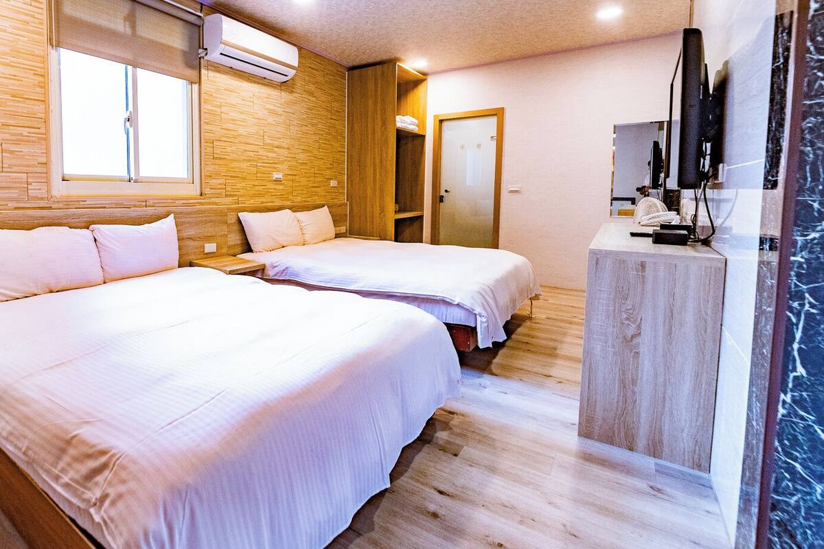 Ein Hotelzimmer mit zwei Betten, Holzwänden, einem großen Fenster und einem Fernseher auf einem Schrank.