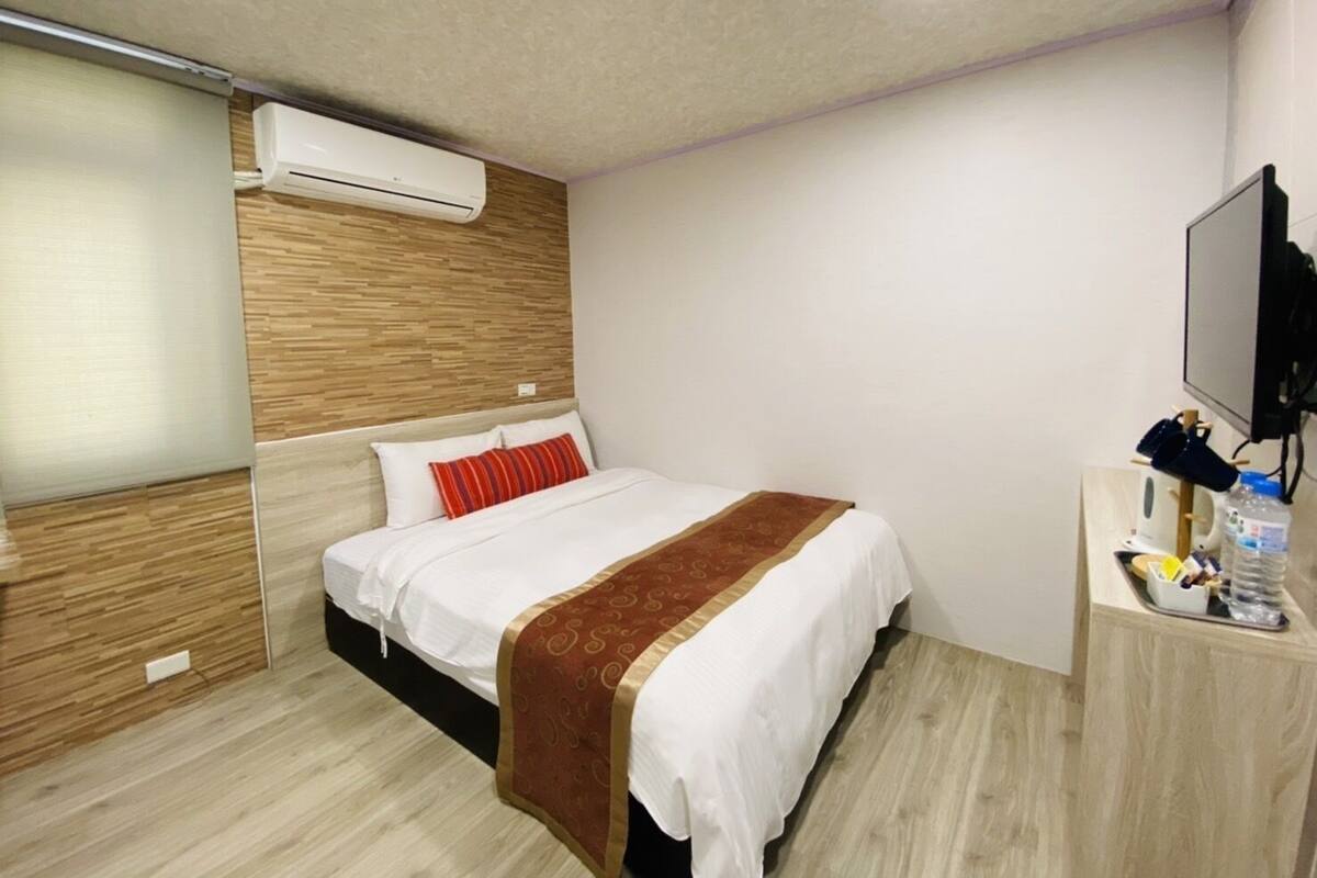 Ein Hotelzimmer mit Bett, Fernseher, Schreibtisch und Wasserflasche sowie einer Klimaanlage.