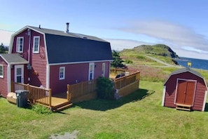 A red two-story house with a wooden deck, a small shed, and a grassy yard.