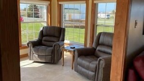 A room with two leather chairs, a small table, and large windows. - Red Sunset Cottage in Twillingate (Twillingate)