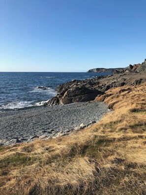 A coastal landscape with rocky terrain and a pebble beach. - Red Sunset Cottage in Twillingate (Twillingate)