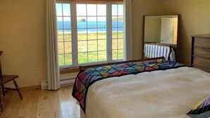 A bedroom with a large bed, a window with curtains, a dresser, and a mirror. - Red Sunset Cottage in Twillingate (Twillingate)