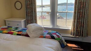Une chambre à coucher avec un lit, une table de chevet, une fenêtre avec des rideaux et une vue sur la mer.