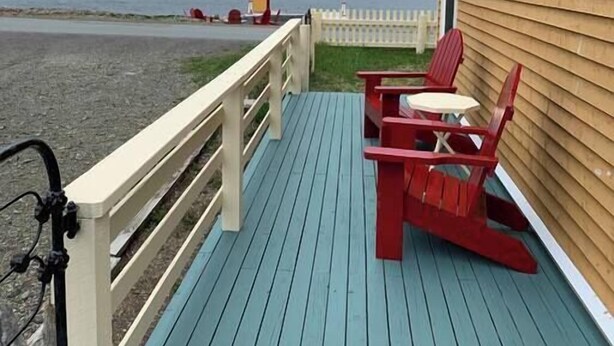 Une terrasse en bois avec une rambarde, une table et deux chaises.