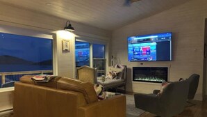A living room with a sofa, armchair, TV, fireplace, and a view of the outdoors. - Spencer Salt-Side Cottage (Salt Harbour) (Herring Neck)