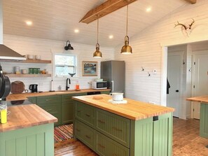 A kitchen with wooden countertops, green cabinets, a central island, pendant lights, a microwave, and a refrigerator.