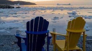 Two Adirondack chairs facing a frozen lake with icebergs, a rocky shoreline, and a distant mountain. - Twilly House (Twillingate)