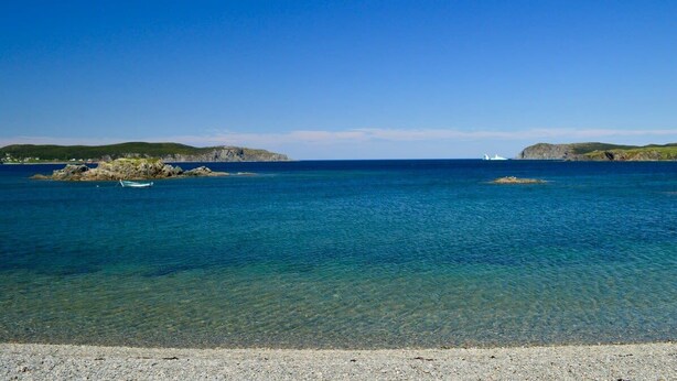 A coastal scene with clear water, a boat, and rocky outcrops. - Twilly House (Twillingate)