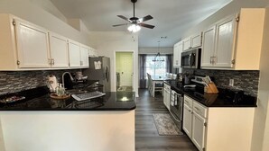 A modern kitchen with white cabinets, a black countertop, a ceiling fan, and a view to the dining area. - The Robin House, Newly Furnished Lake Retreat Near Tybee Island & Savannah (Wilmington Island)