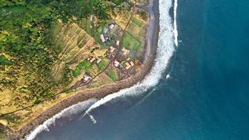 An aerial view of a coastal area with terraced fields and a small cluster of buildings near the shoreline.
